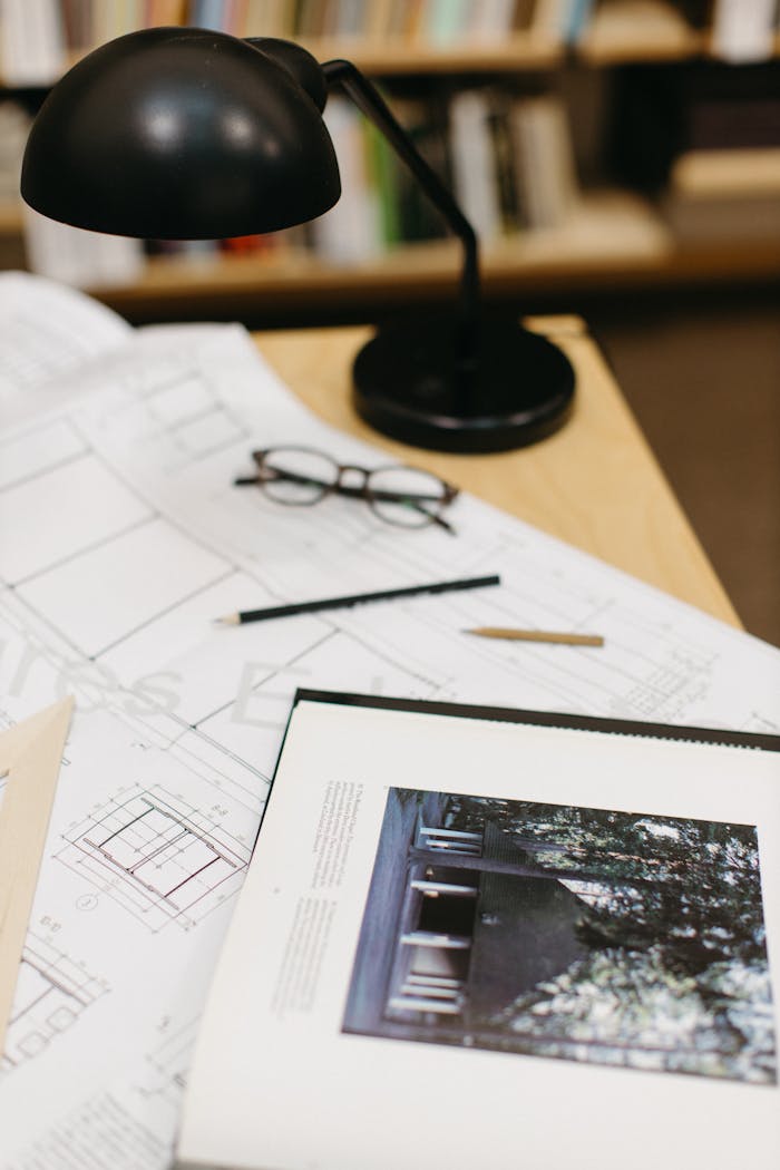 Architect's workspace with blueprints, a book, glasses, and a lamp.